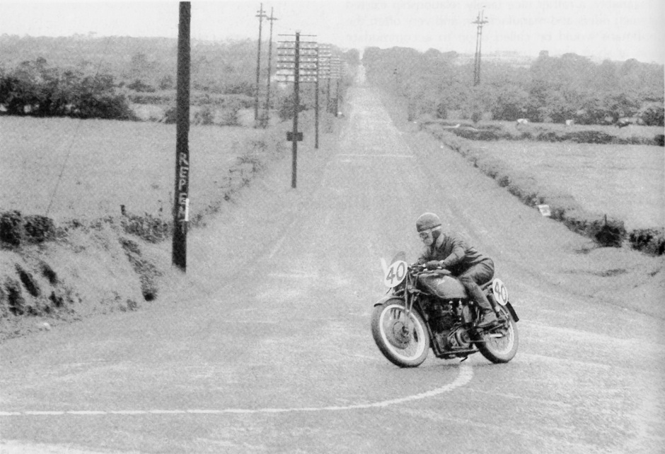 Arthur Wheeler at the end of Dundrod’s straight on a works DOHC 250 in 1952, note the enormous 8 gallon aluminium tank, held on with a third tube from the top of the steering head to the top of the seat tube, passing straight through the centre of the tank. Also of note is the lack of friction dampers on the lower arms connecting the fork yoke to the girders. These forks were apparently especially shortened to cope with the lower steering head position and the use of a 19 inch front wheel. Although I have never laid eyes on such they are said to have needle roller spindles and a hydraulic damping unit, and the bikes handled superbly.
